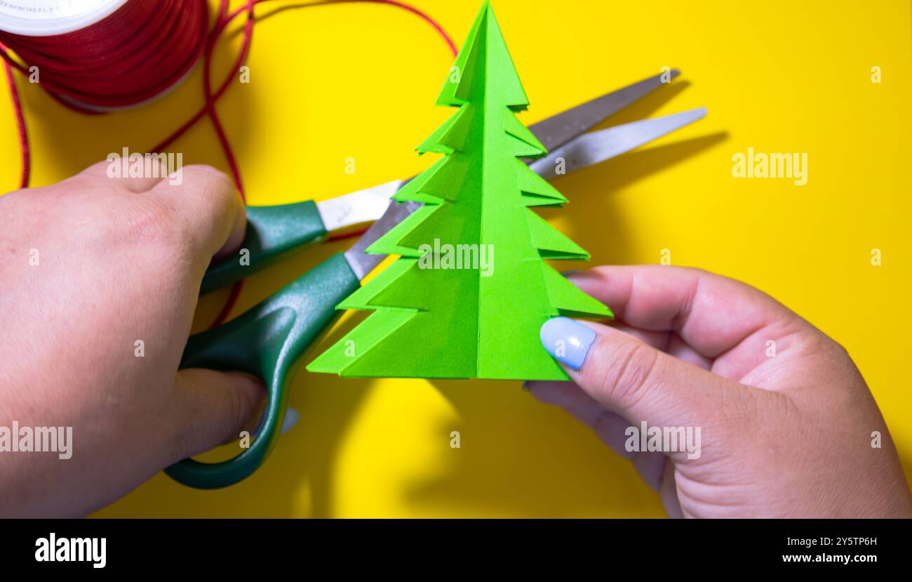 Femme fabriquant de l'artisanat pour les décorations de Noël sur un fond jaune avec un fil décoratif de Noël et des ciseaux Banque D'Images