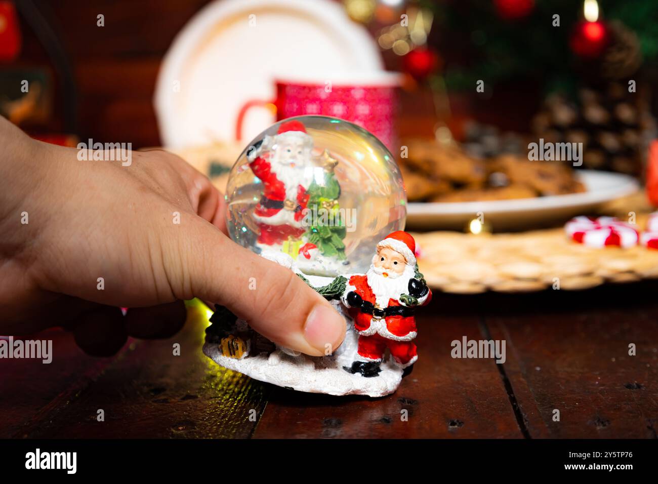 Main masculine tenant la boule de verre de Noël décorée avec le Père Noël sur un fond en bois et décorations de Noël défocalisées Banque D'Images