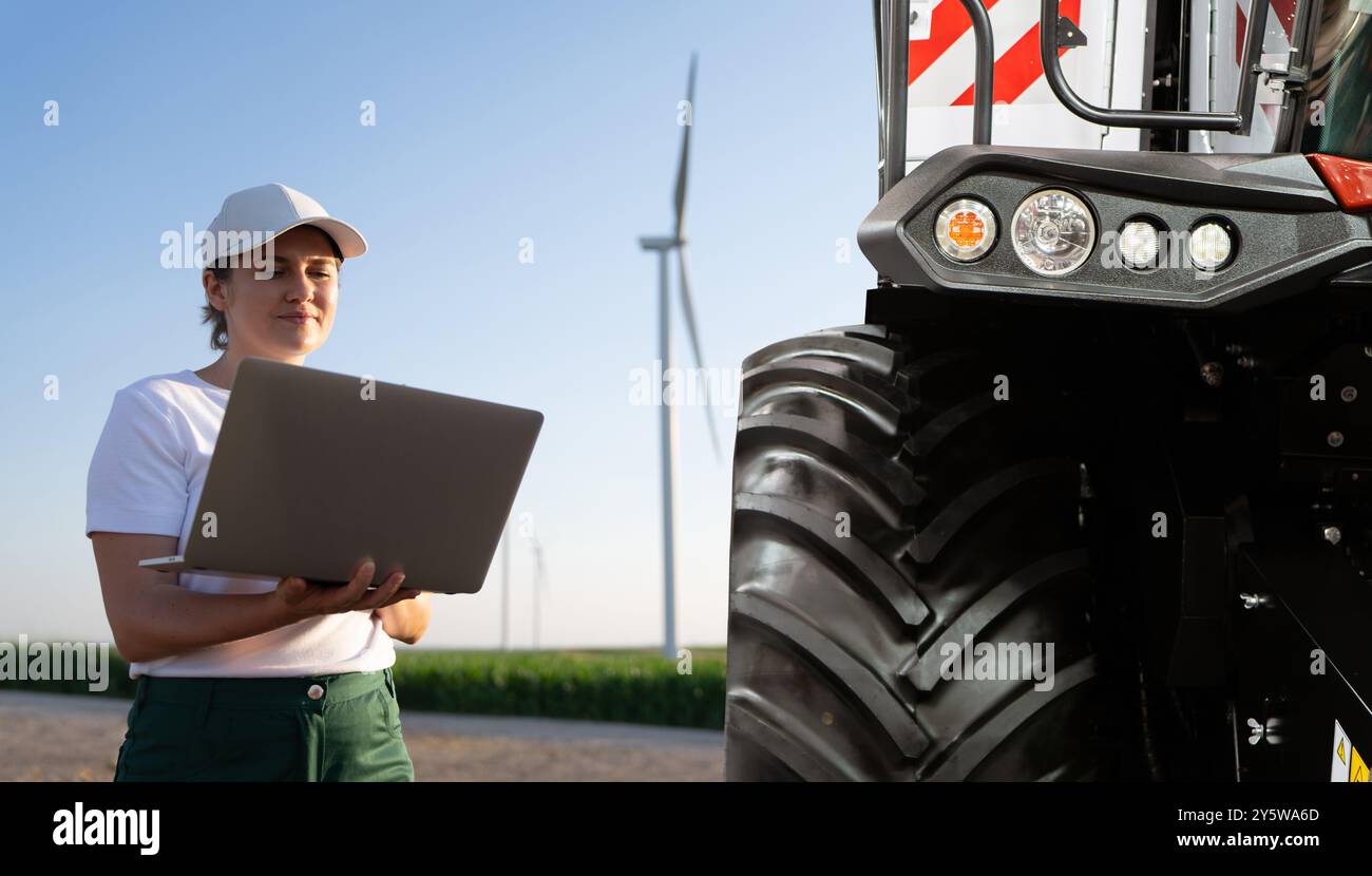 Femme agricultrice avec un ordinateur portable à côté d'un tracteur agricole... Banque D'Images