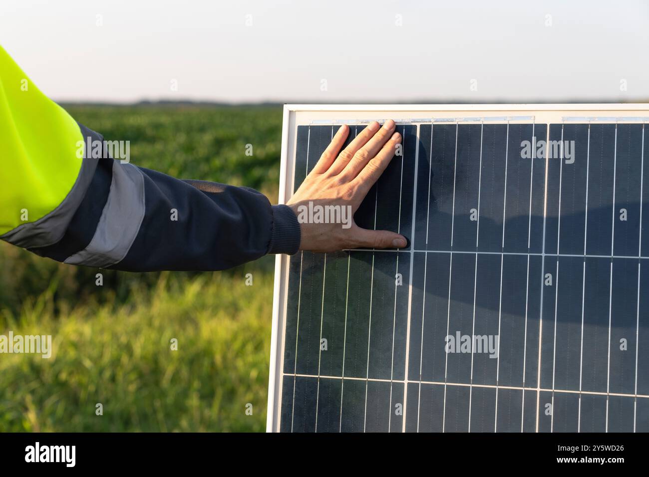 Gros plan d'une main touchant un panneau solaire au coucher du soleil. Banque D'Images