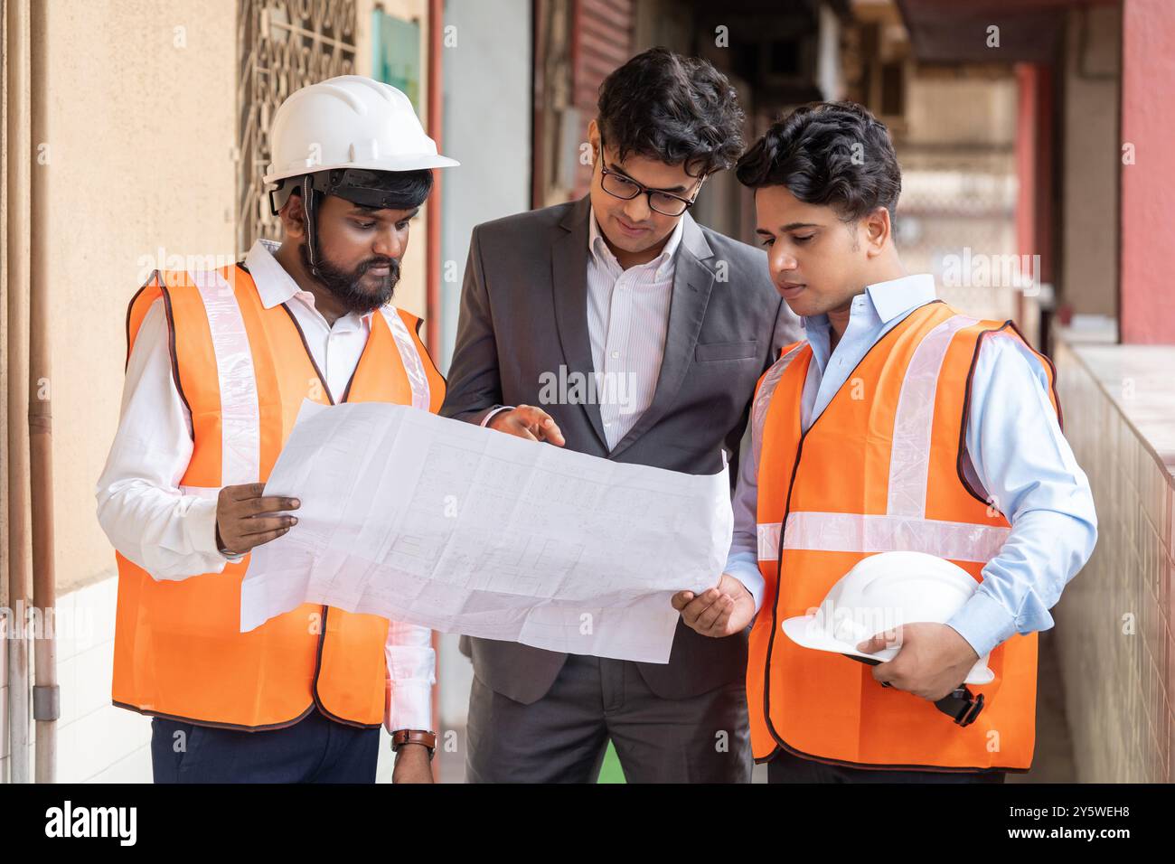 Un ingénieur de projet, un superviseur de site et un ingénieur électricien sont profondément engagés dans une discussion détaillée sur un site de construction industrielle se concentrant sur o Banque D'Images