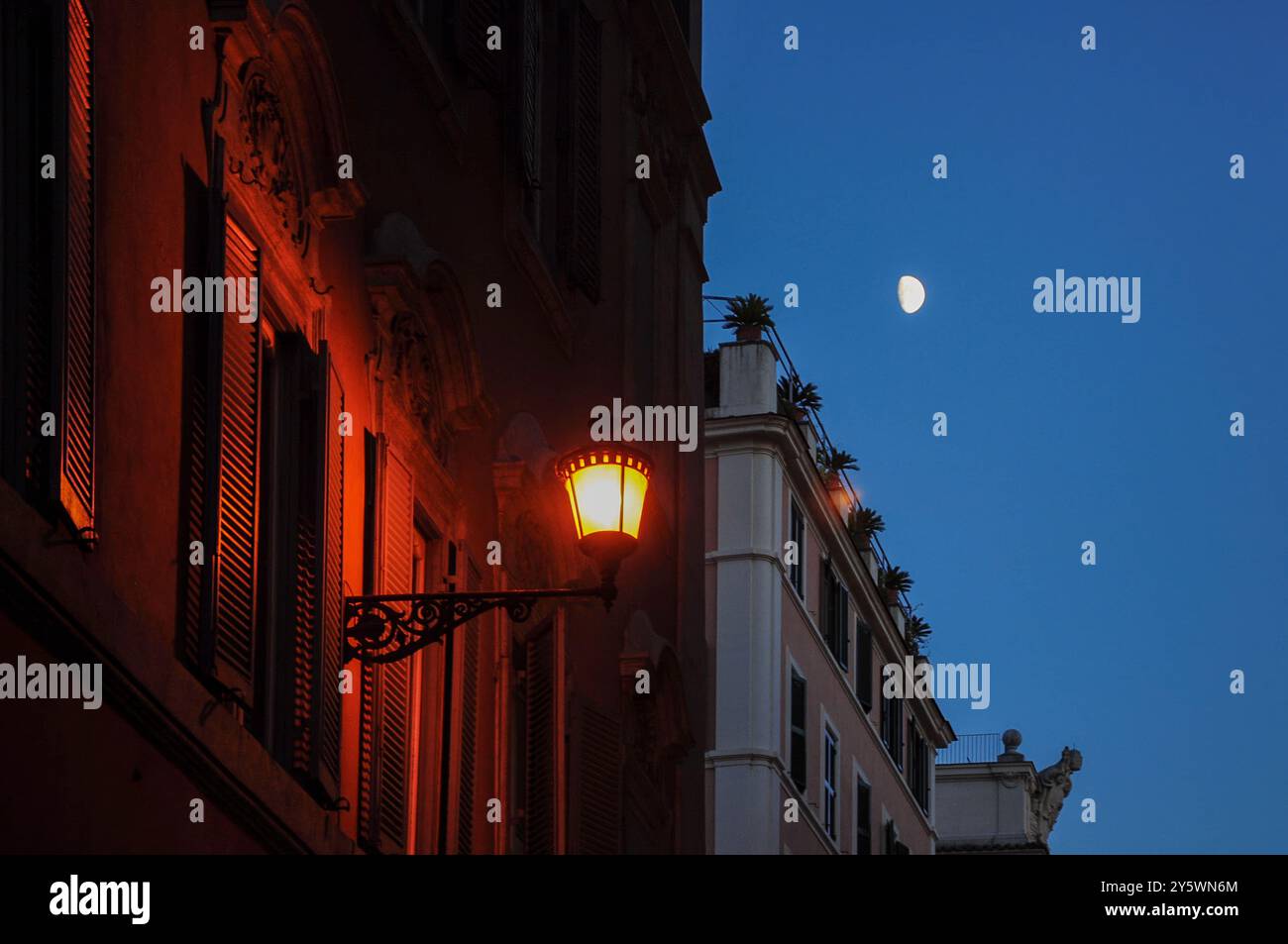 La lanterne de rue éclaire de vieux bâtiments au crépuscule sous ciel clair avec la lune Banque D'Images