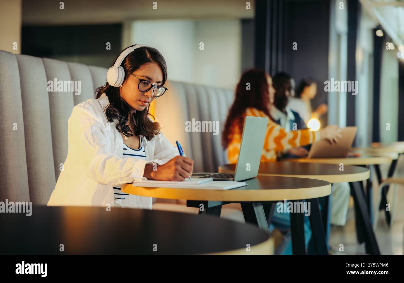 Des collègues concentrés travaillant dans un espace de coworking moderne, avec des écouteurs et des ordinateurs portables, mettant en valeur la concentration et la productivité dans un bureau partagé envi Banque D'Images