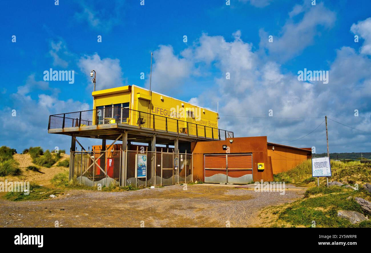Un poste de sauveteur surélevé jaune vif se trouve sur une plage entourée de dunes de sable et d'herbe Banque D'Images