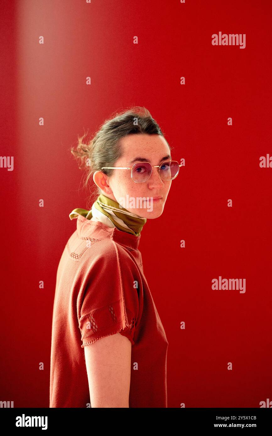 Femme avec des lunettes regardant par-dessus l'épaule sur un fond rouge. Banque D'Images