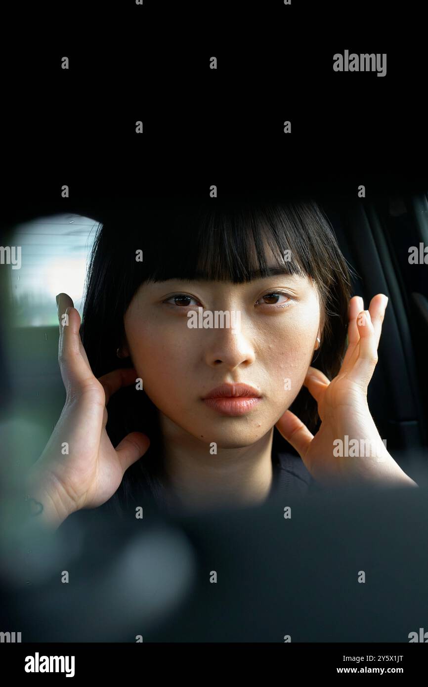 Portrait en gros plan d'une jeune femme avec une expression sereine reposant sa tête sur ses mains à l'intérieur d'une voiture. Banque D'Images