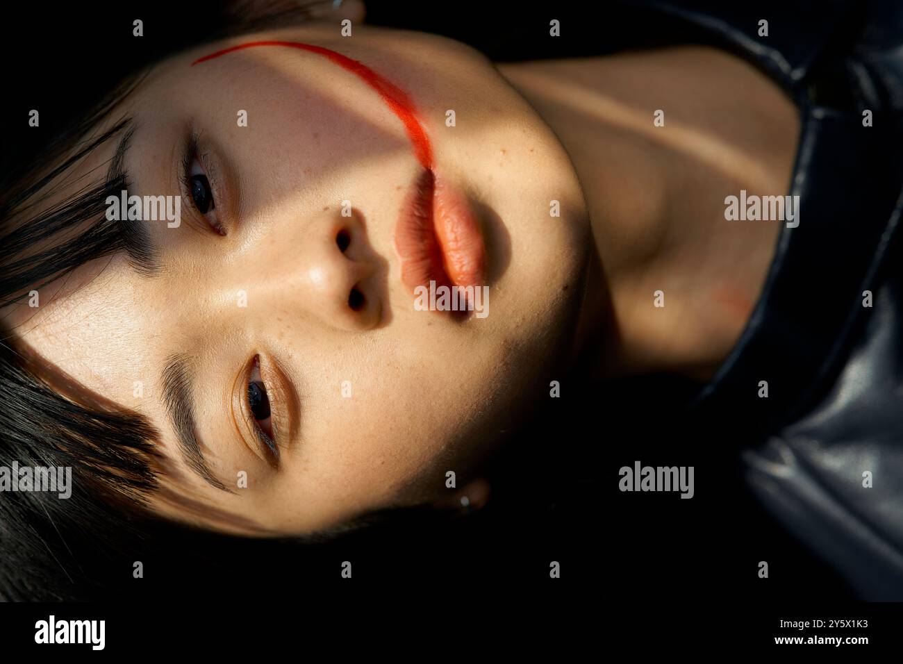 Gros plan du visage d'une personne avec la lumière du soleil projetant des ombres, avec une ligne rouge distincte sur la joue. Banque D'Images