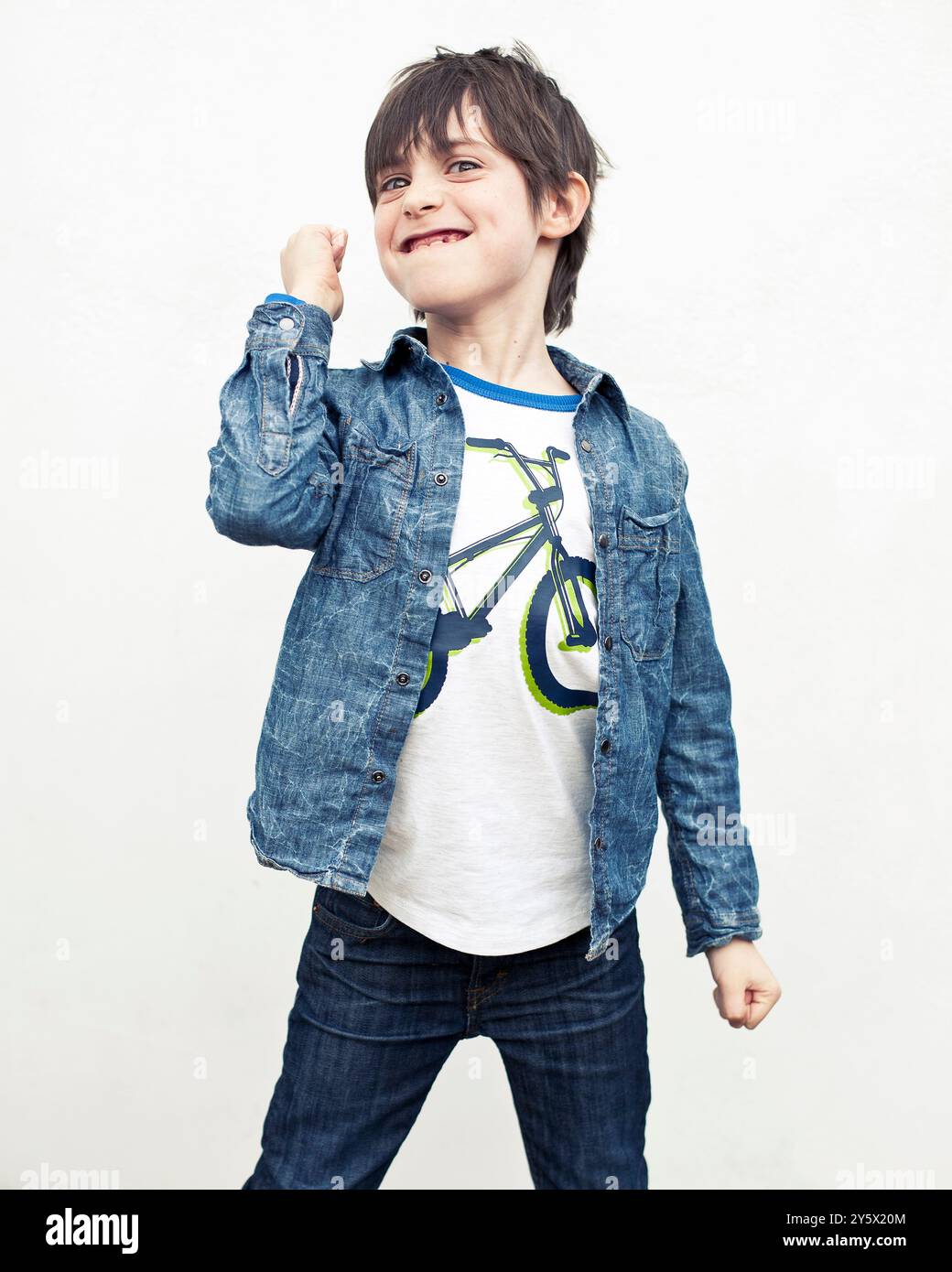 Garçon souriant dans une veste en denim posant avec un geste de pompe de poing sur un fond blanc. Banque D'Images