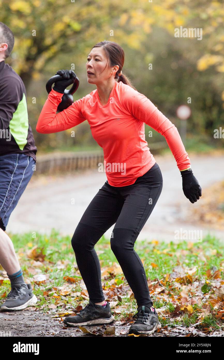 Femme en vêtements de sport orange et gants se concentrant sur sa technique de course dans un parc en automne. Banque D'Images