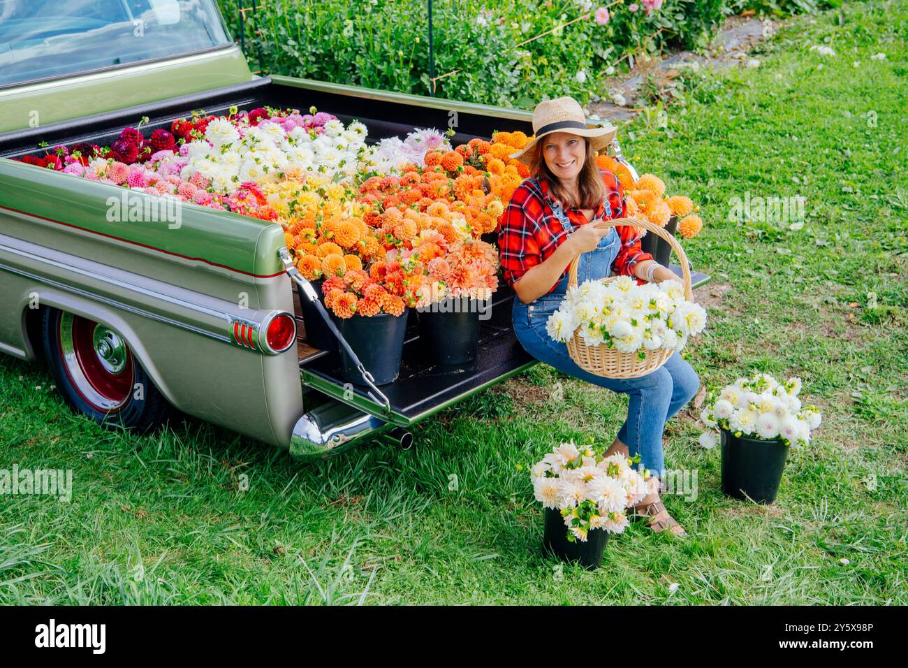 Femme souriante dans un chapeau arrangeant des bouquets de fleurs colorées à l'arrière d'une camionnette vintage par une journée ensoleillée. Banque D'Images
