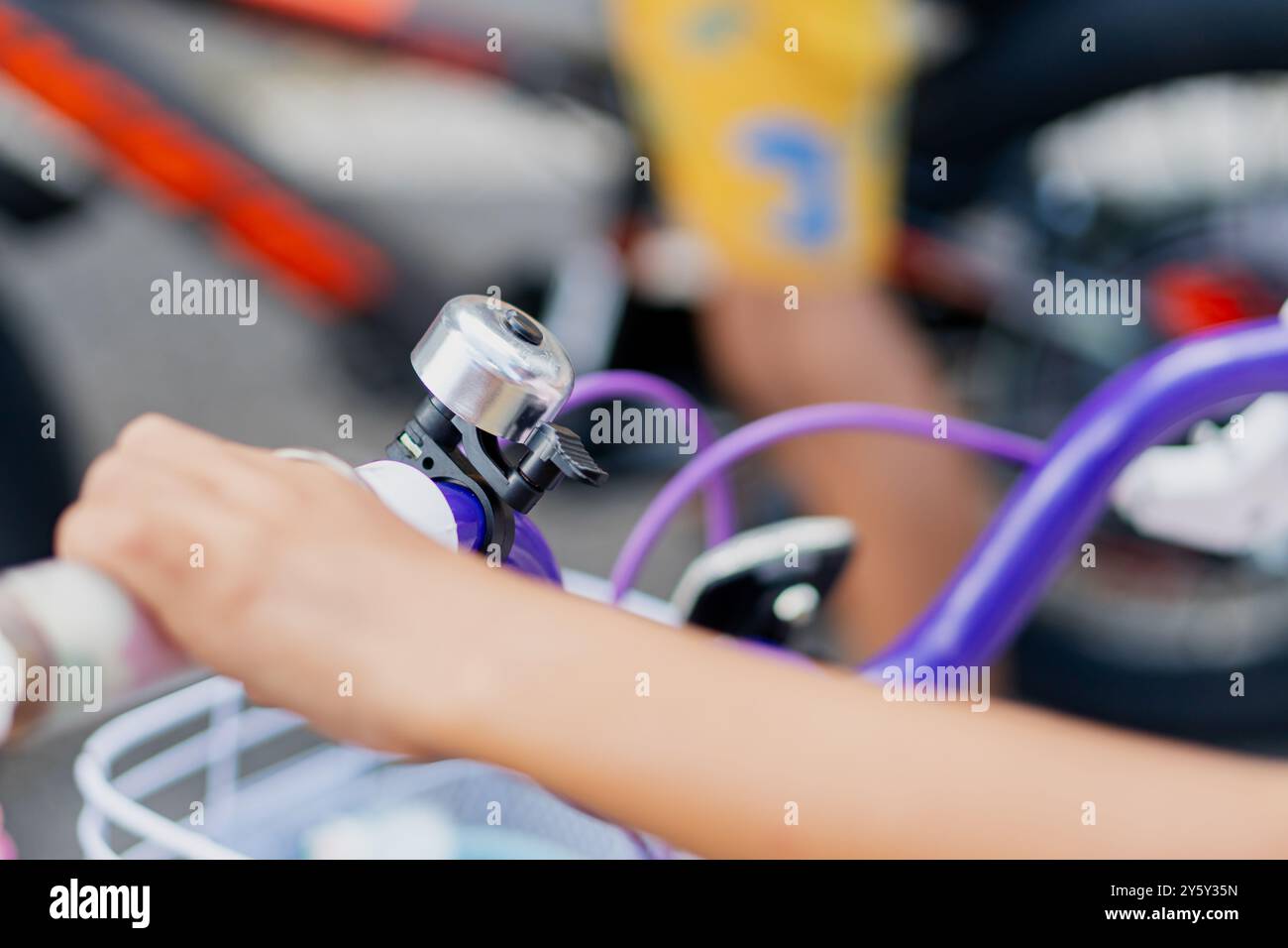 Une main d'enfant sur le guidon d'un vélo violet, mettant en valeur l'activité et le jeu en plein air. Une cloche argentée est attachée à la poignée, soulignant le bi Banque D'Images