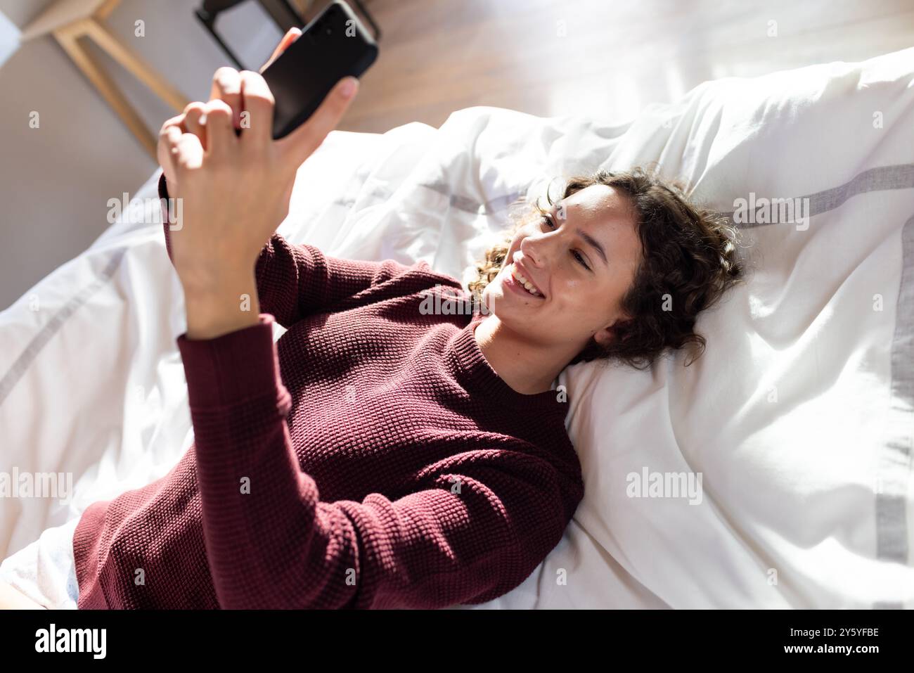 Couché sur le lit, femme souriante et utilisant un smartphone pour la détente Banque D'Images