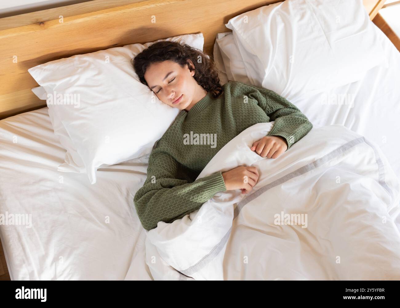Dormir paisiblement, femme se reposant dans le lit avec des draps blancs et un pull vert Banque D'Images