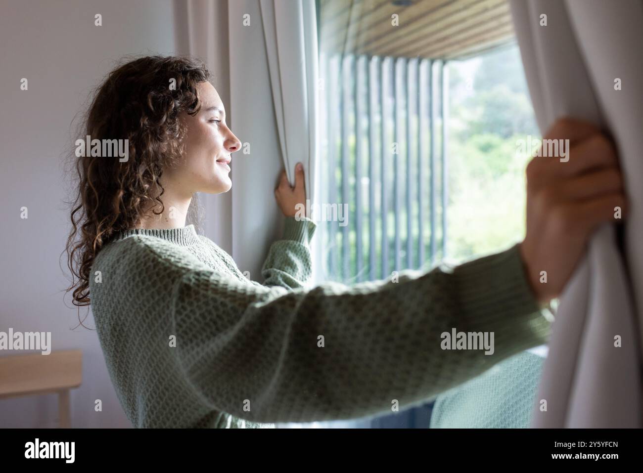 Rideaux d'ouverture, femme profitant de la lumière du soleil du matin et de l'air frais dans une chambre confortable Banque D'Images