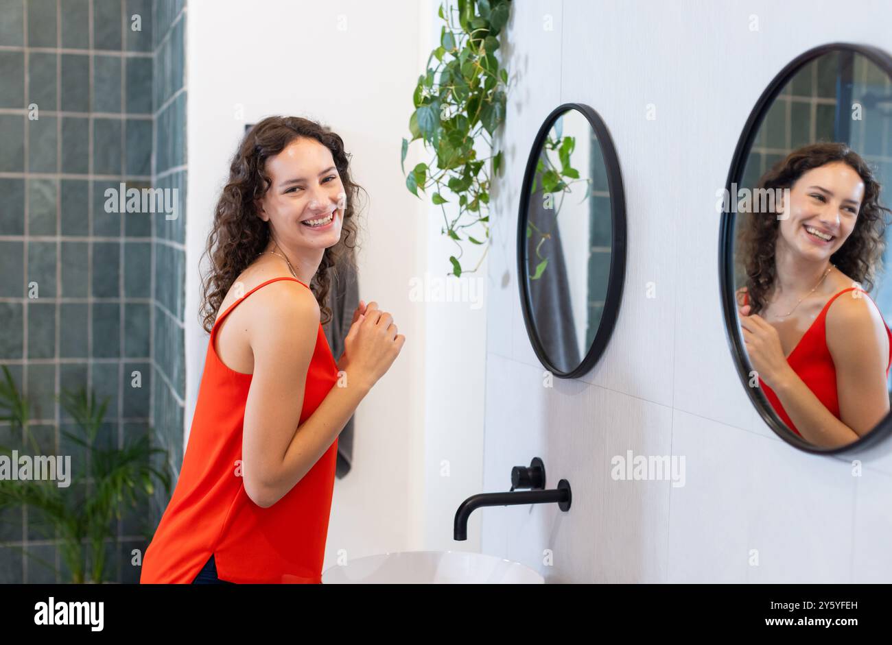 Femme souriante dans la salle de bain regardant le miroir, appréciant la routine de soins personnels Banque D'Images