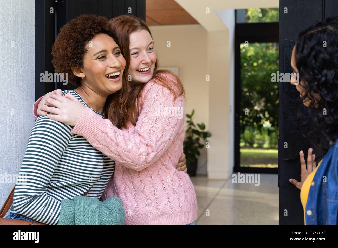 Embrassant et souriant, deux amies femmes se saluent à l'entrée de la maison Banque D'Images