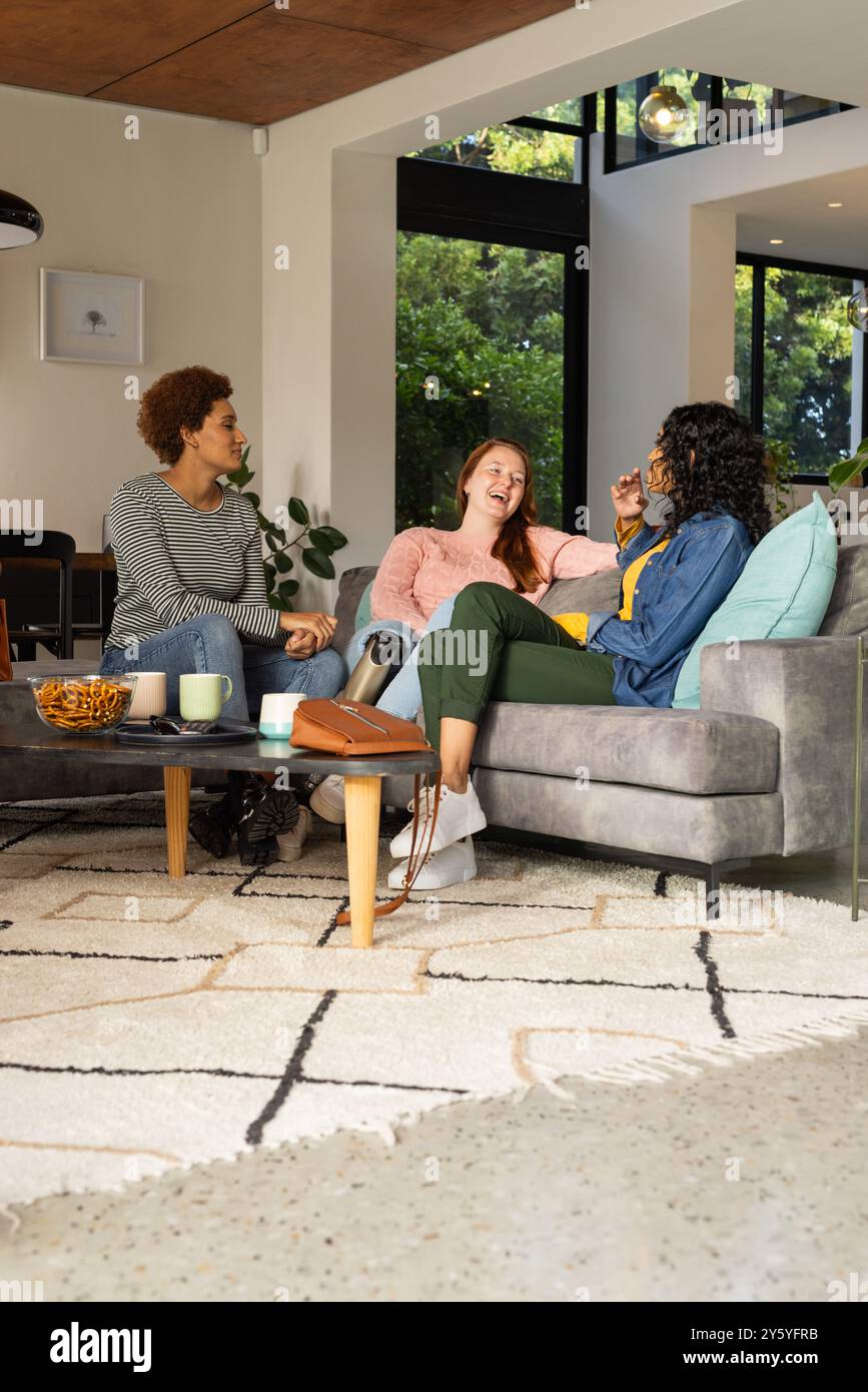 Détente sur le canapé, diverses femmes amis riant et parlant dans le salon confortable Banque D'Images