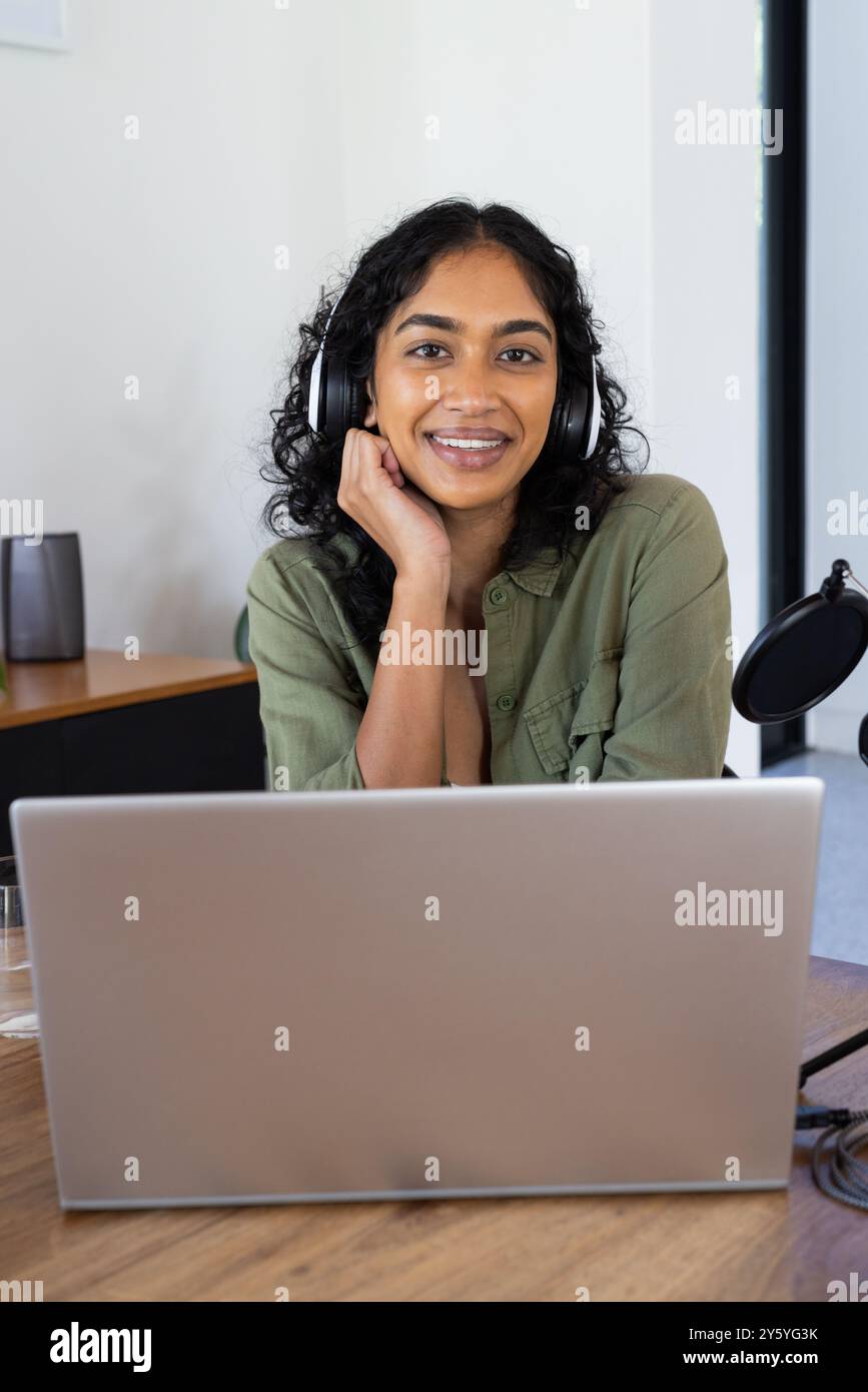 Femme souriante portant des écouteurs à l'aide d'un ordinateur portable pour réunion en ligne à la maison, espace de copie Banque D'Images