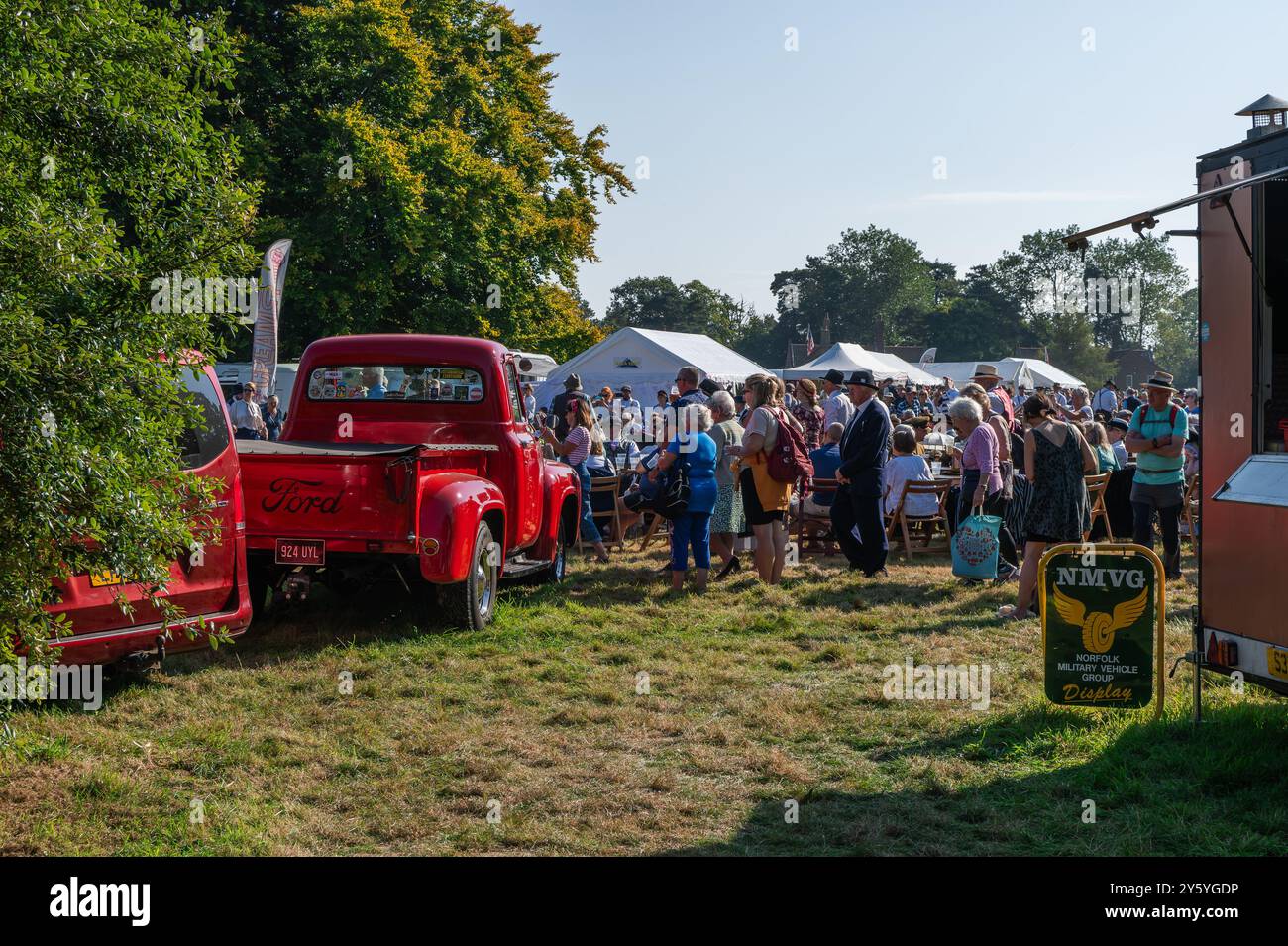 Holt, Norfolk, Royaume-Uni - 21 SEPTEMBRE 2024 : les gens sur l'herbe participant au week-end des années 1940 à côté de camionnette rouge Ford vintage Banque D'Images