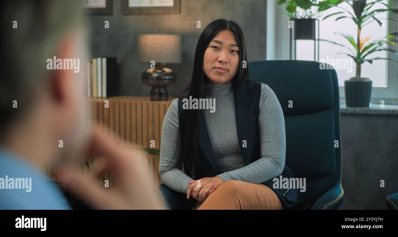 Jeune femme asiatique parle de conflit familial, discute des problèmes relationnels lors de la consultation avec un psychothérapeute. Au premier plan, le psychologue non focalisé écoute le patient pendant la thérapie de couple. Banque D'Images