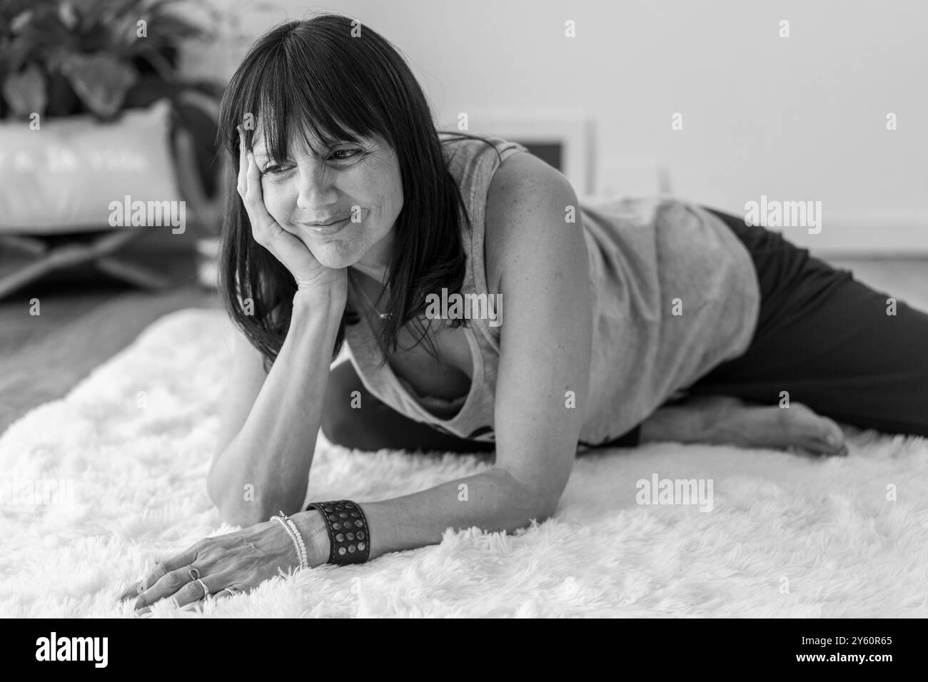 Charmant portrait d'une femme mi-adulte confortablement couchée sur un tapis blanc doux dans son studio de yoga tranquille. Banque D'Images