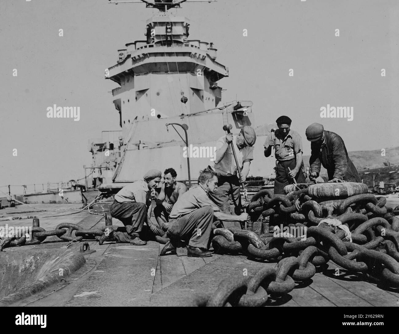 Les travaux ont commencé hier sur le démantèlement du cuirassé vétéran 'Warease', qui s'est échoué à Prussia Cove, Cornouailles, alors qu'il se rendait au chantier naval de Breaker. Le navire a été acheté pour un chiffre non divulgué par MM. R.H.Bennett et A.J.Brewis, de Bristol. Le démantèlement, qui se fera sur place, devrait durer environ trois ans. Beaucoup d'acier précieux, d'équipement électrique, de machines et de bois seront récupérés du grand vieux navire. Images : les ouvriers font un départ sur les chaînes d'ancre de 'Warease' à Prussia Cove hier. 2 septembre 1947 Banque D'Images