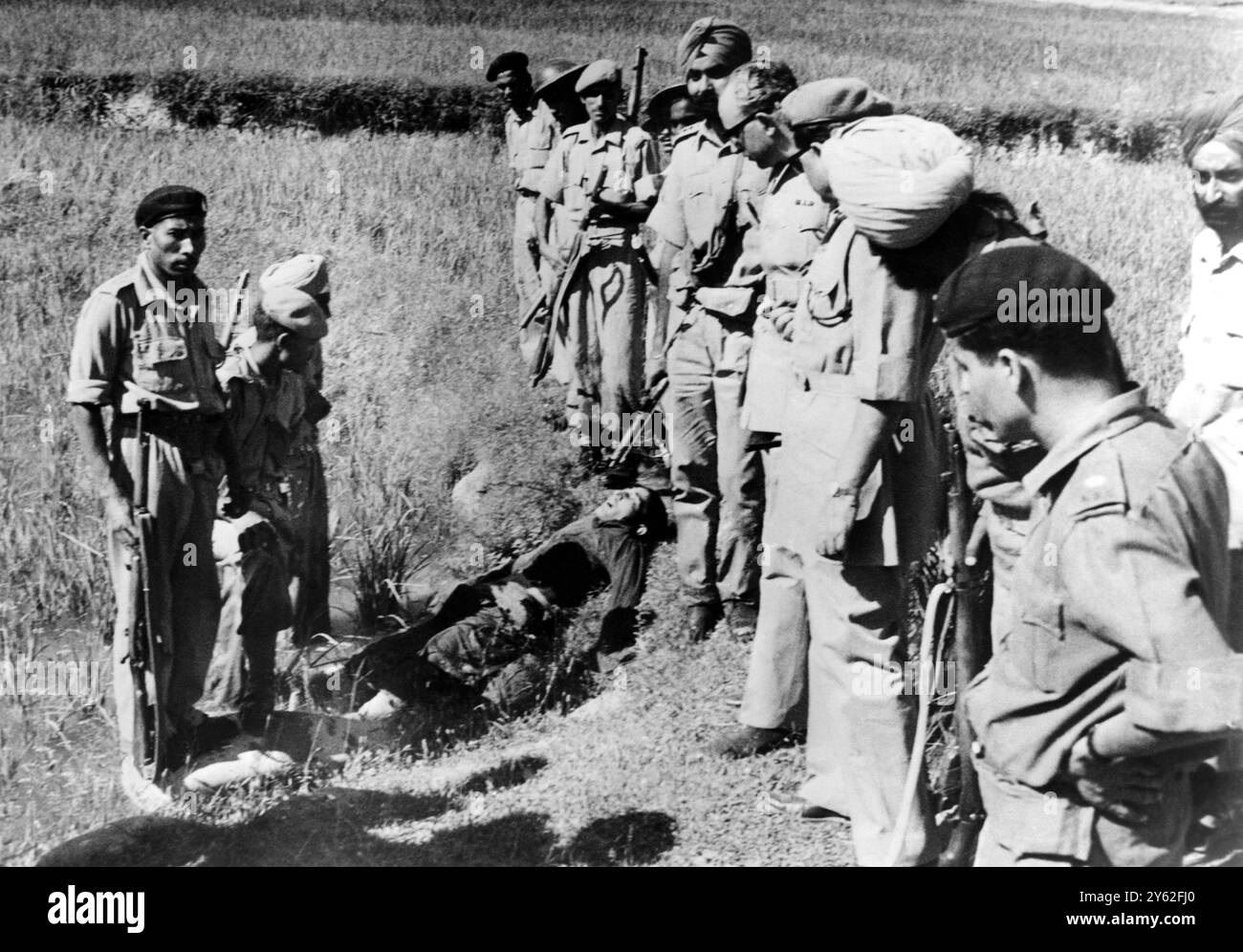 Les forces de sécurité indiennes se tiennent au-dessus du corps d'un soldat mort , soupçonné d'être un infiltré pakistanais , gisant dans une rizière ici le 18 août 1965. Le soldat a été abattu par les forces indiennes alors qu'il « essayait de faire sauter un pont » que les forces gardaient. Srinigar , Cachemire Banque D'Images