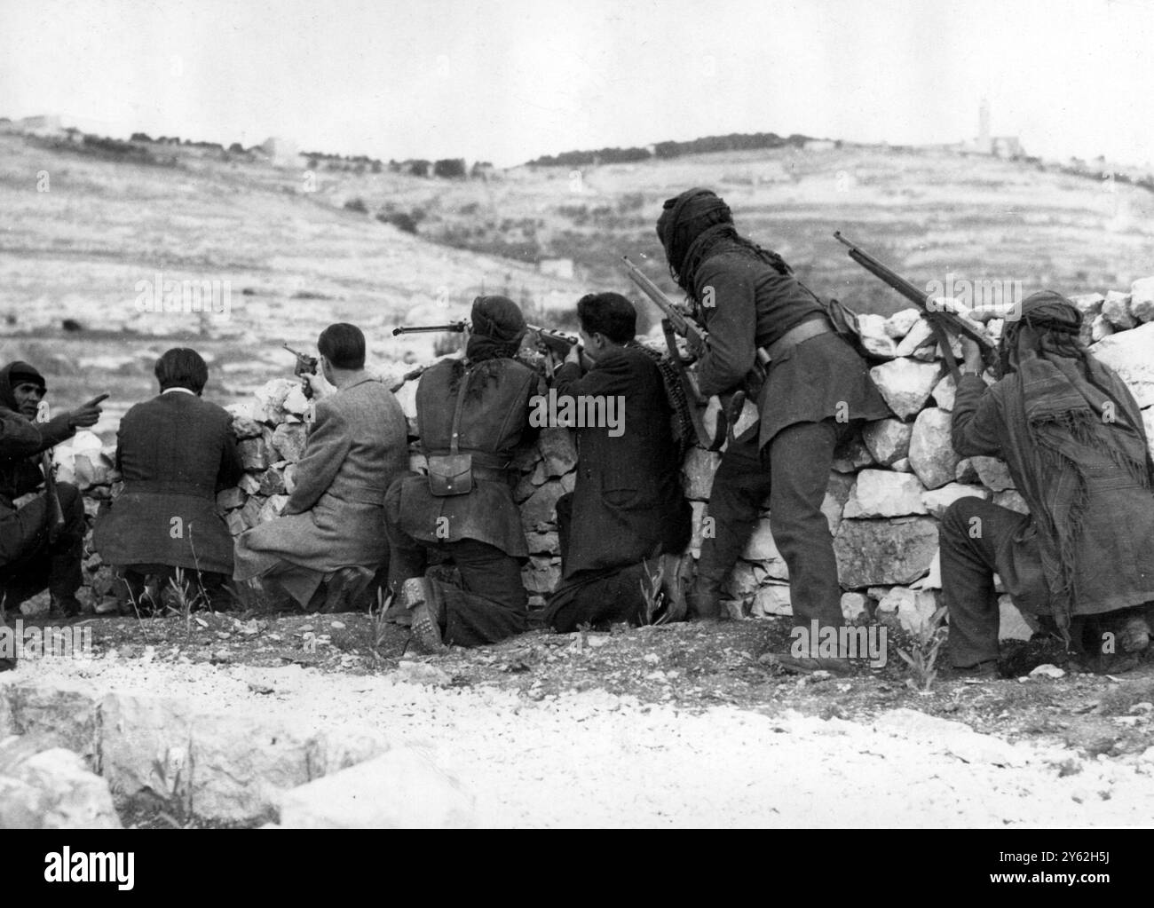 Photo prise sur le Mont des oliviers surplombant Jérusalem alors que les Arabes, derrière la couverture d'un mur de pierre, regardaient les tireurs d'élite juifs de la vieille ville de Jérusalem qui a maintenant été capturée par la Légion arabe . Les Arabes se préparent maintenant à un assaut contre le labyrinthe de rues et de bâtiments en pierre dans les nouveaux quartiers de Jérusalem. Expositions de photos ; Arabes avec des fusils à la veille prête pour les tireurs d'élite du Mont des oliviers dans la région de l'Université hébraïque. 31 mai 1948 Banque D'Images