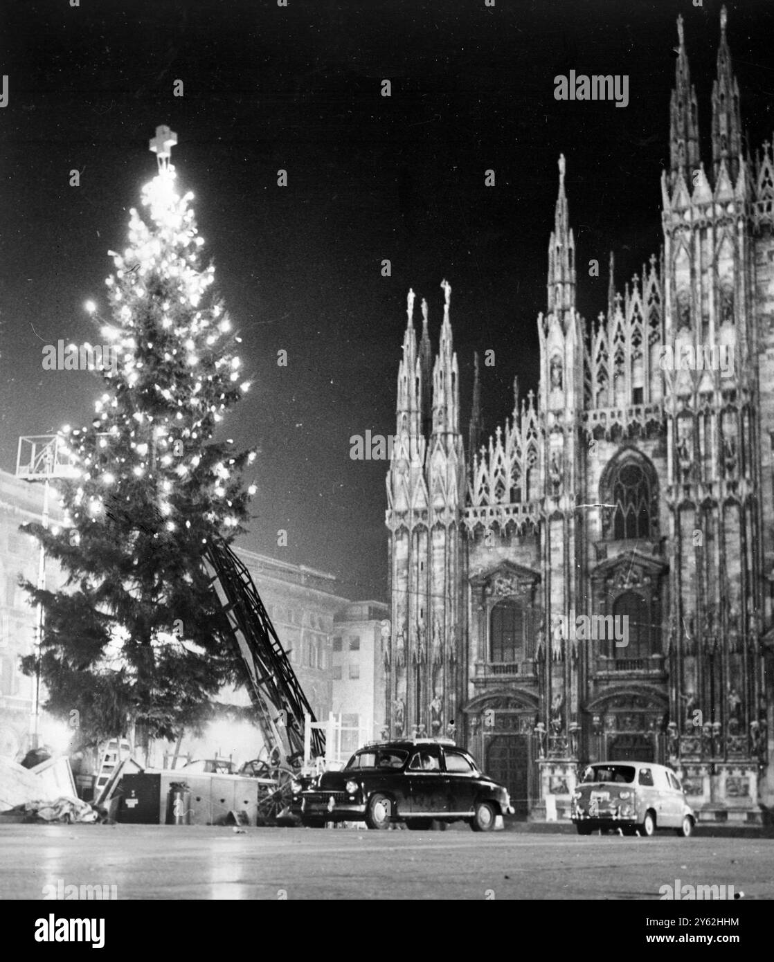 Milan , Italie . Ajout d'un nouveau sommet aux nombreuses spires gothiques du célèbre Duomo ( cathédrale ) de Milan , Un arbre de Noël haut brille de lumières comme il est élevé sur la place principale . L'arbre a été 'planté' par la Croix-Rouge italienne et portera des cadeaux pour les pauvres . 11 décembre 1959 Banque D'Images