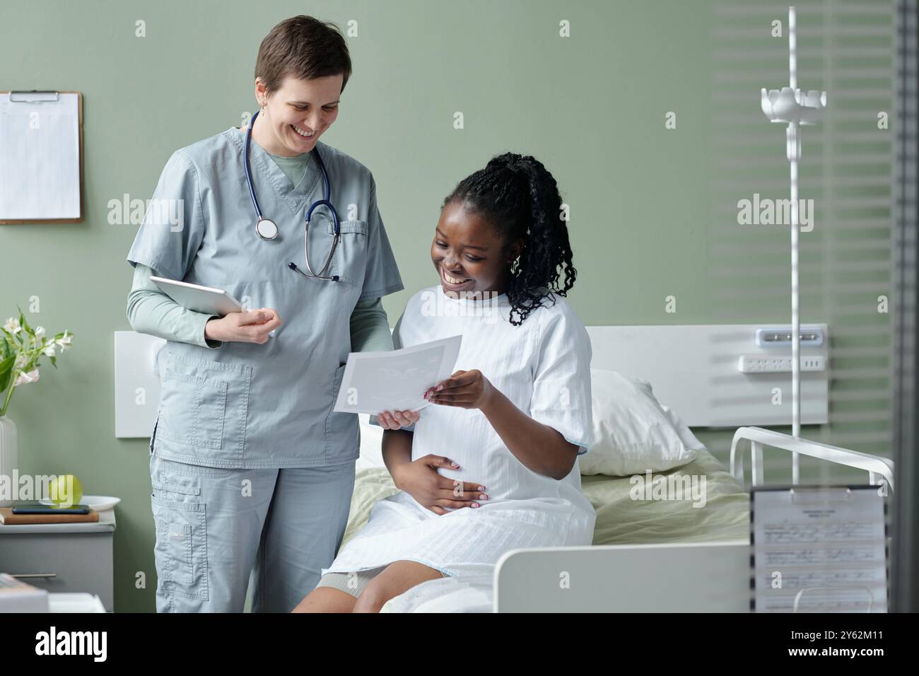 Infirmière s'engageant avec le patient dans la chambre d'hôpital, souriante tout en examinant les documents infirmière debout à côté du lit, patient assis Banque D'Images