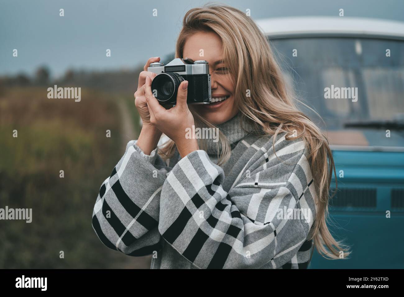 Cool shot ! Jeune femme attrayante photographiant et souriant tout en se tenant à l'extérieur avec le mini van de style rétro bleu en arrière-plan Banque D'Images