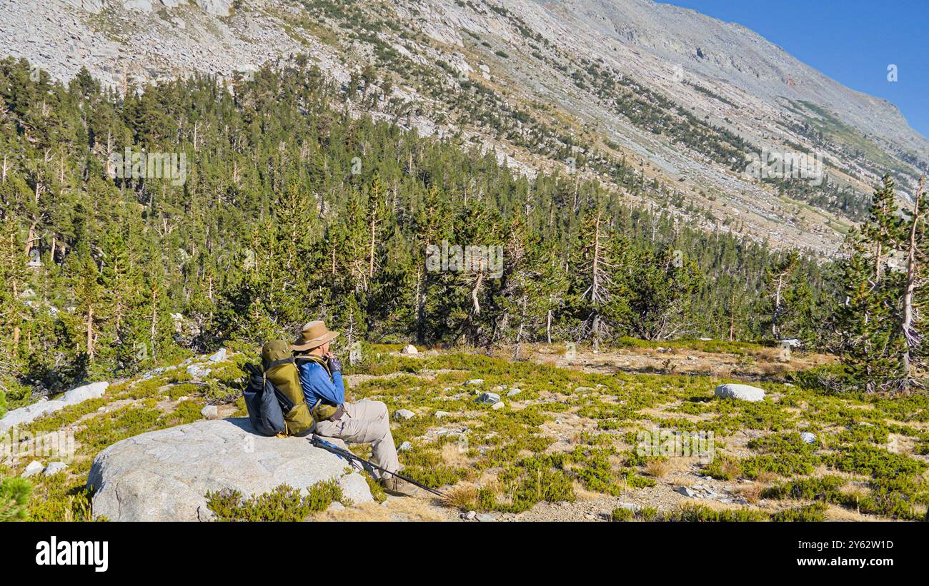 Un randonneur s'assoit sur un rocher près de High Sierra Trial. Banque D'Images