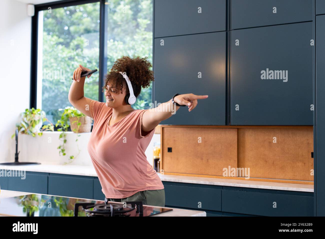 Danse dans la cuisine, femme de taille plus appréciant la musique avec des écouteurs et smartphone, à la maison, à la maison Banque D'Images