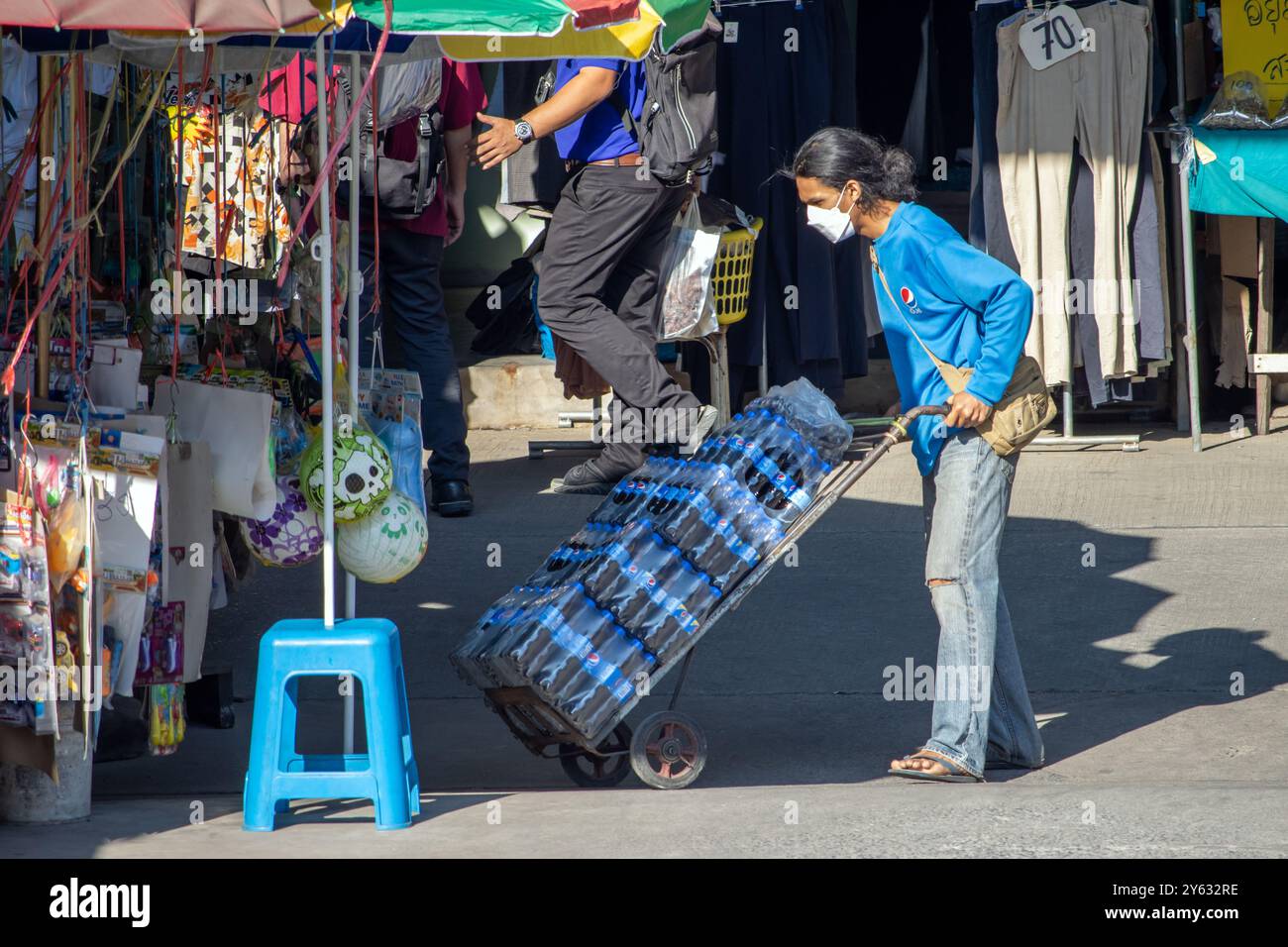 SAMUT PRAKAN, THAÏLANDE, 08 février 2023, Un ouvrier pousse un chariot rempli de bouteilles de cola Banque D'Images