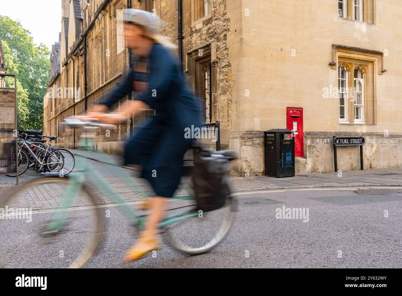 Oxford Royaume-Uni - 24 juillet 2024 ; image floue d'une femme faisant du vélo devant un coin de Brasenose Land et Turn Street avec une boîte aux lettres rouge traditionnelle à Wal Banque D'Images