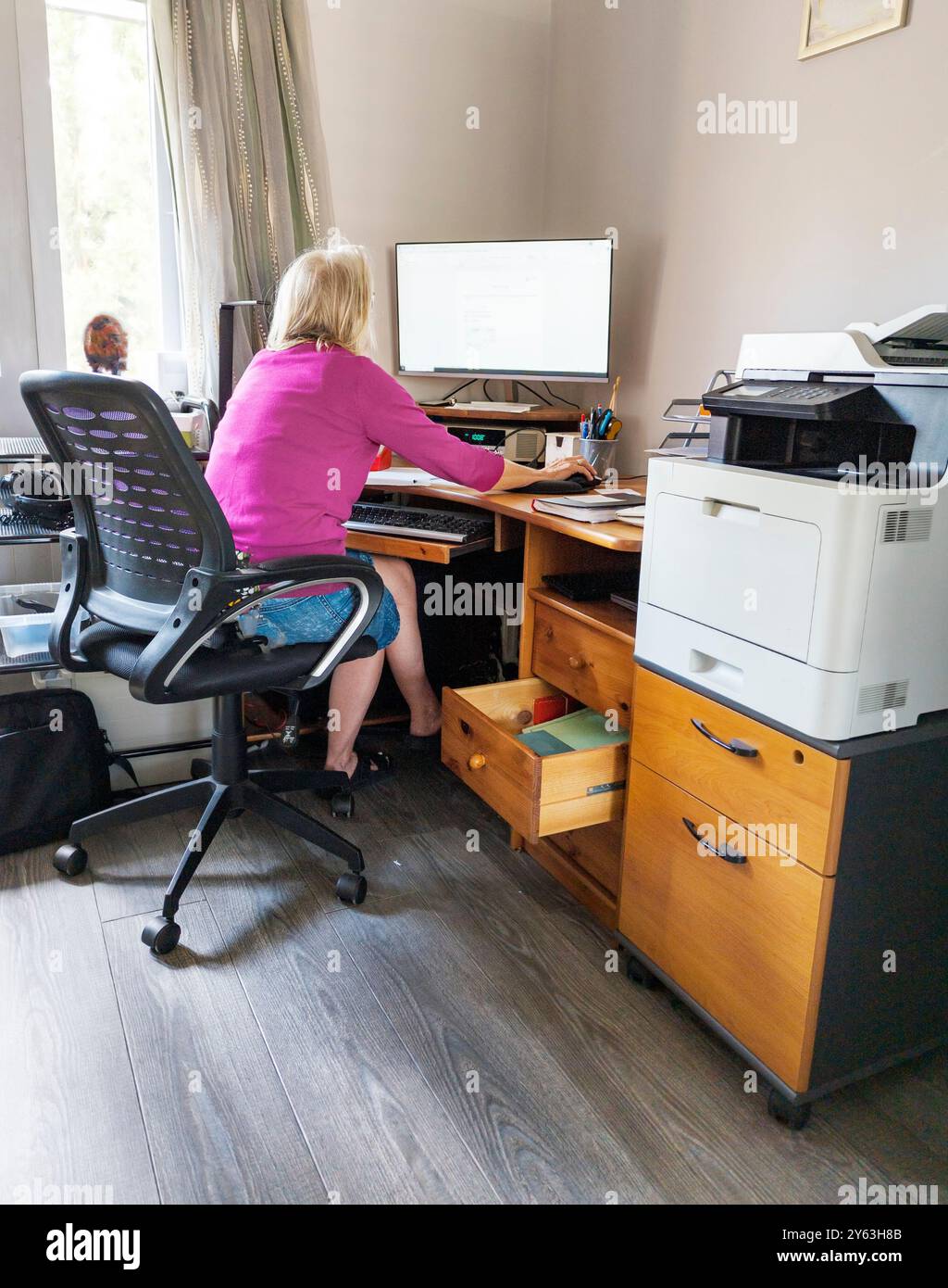 Une travailleuse à domicile, offrant des services de secrétariat et d'administration, portant des lunettes, communiquant avec les clients, à son ordinateur de bureau à domicile, dans son espace de travail Banque D'Images