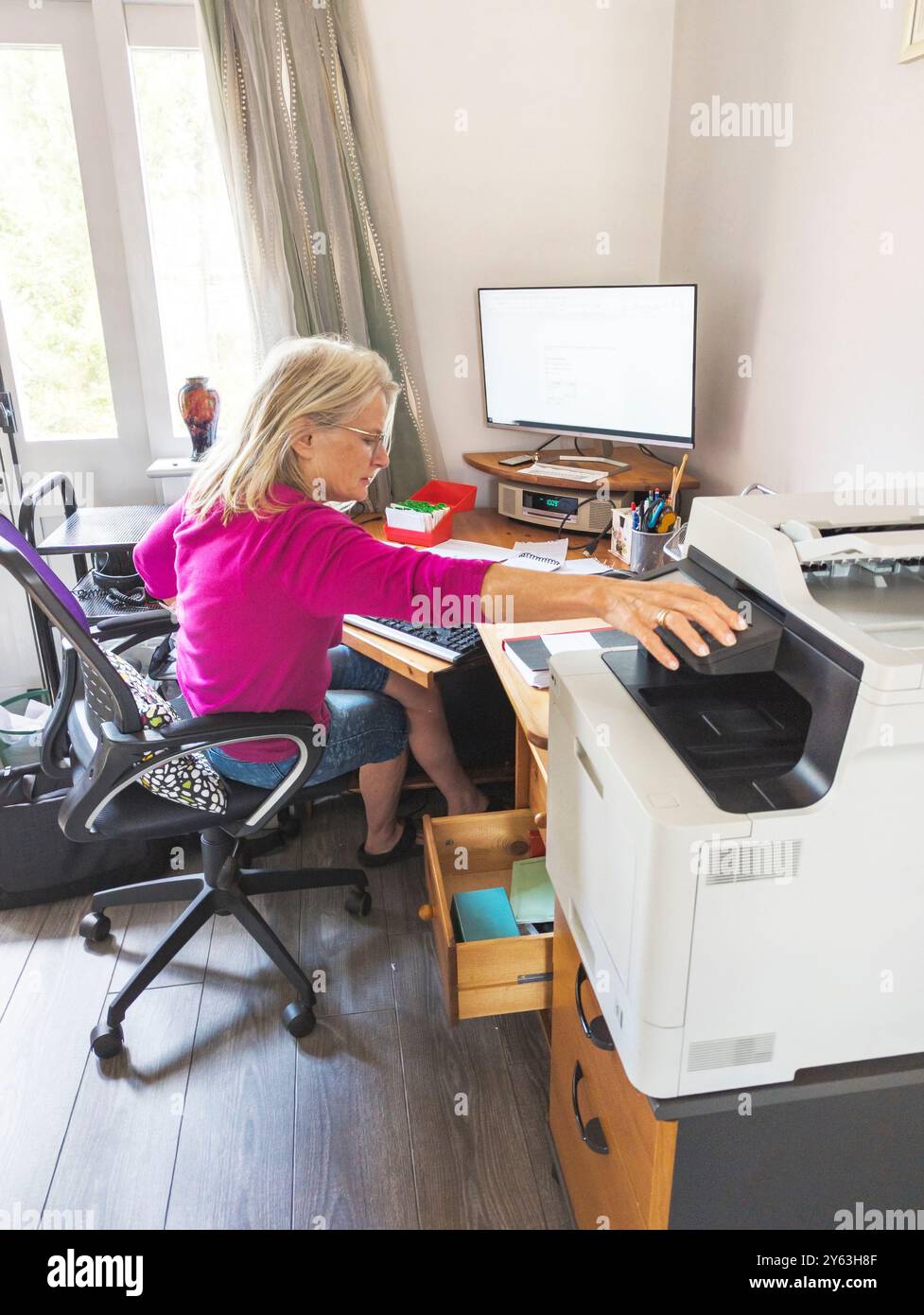 Une travailleuse à domicile, offrant des services de secrétariat et d'administration, portant des lunettes, communiquant avec les clients, à son ordinateur de bureau à domicile, dans son espace de travail Banque D'Images