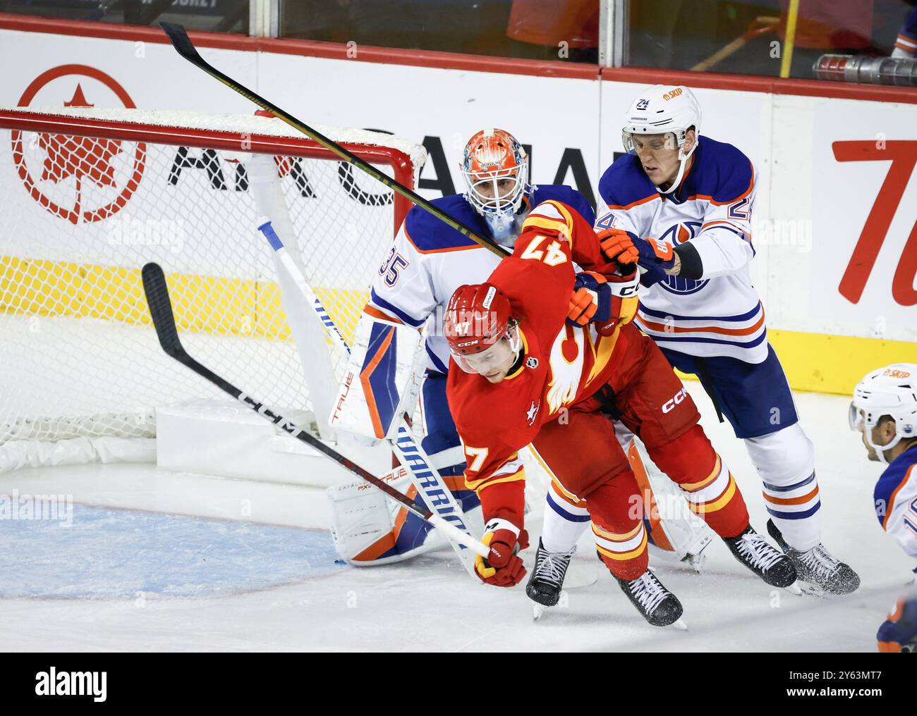 Edmonton Oilers' Travis Dermott (24) checks Calgary Flames' Connor Zary (47) as Oilers goalie Olivier Rodrigue (35) looks on during second-period preseason NHL hockey game action in Calgary, Alberta, Monday, Sept. 23, 2024. (Jeff McIntosh/The Canadian Press via AP) Banque D'Images