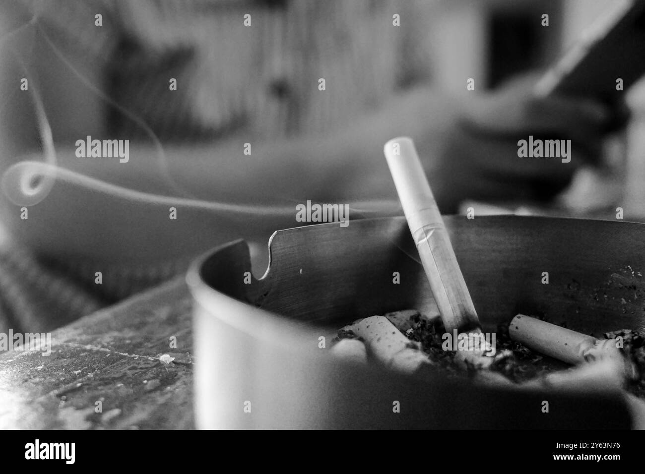 Cigarette brûlée dans un cendrier avec une femme sur le fond assis tout en tenant le téléphone dans un café Banque D'Images