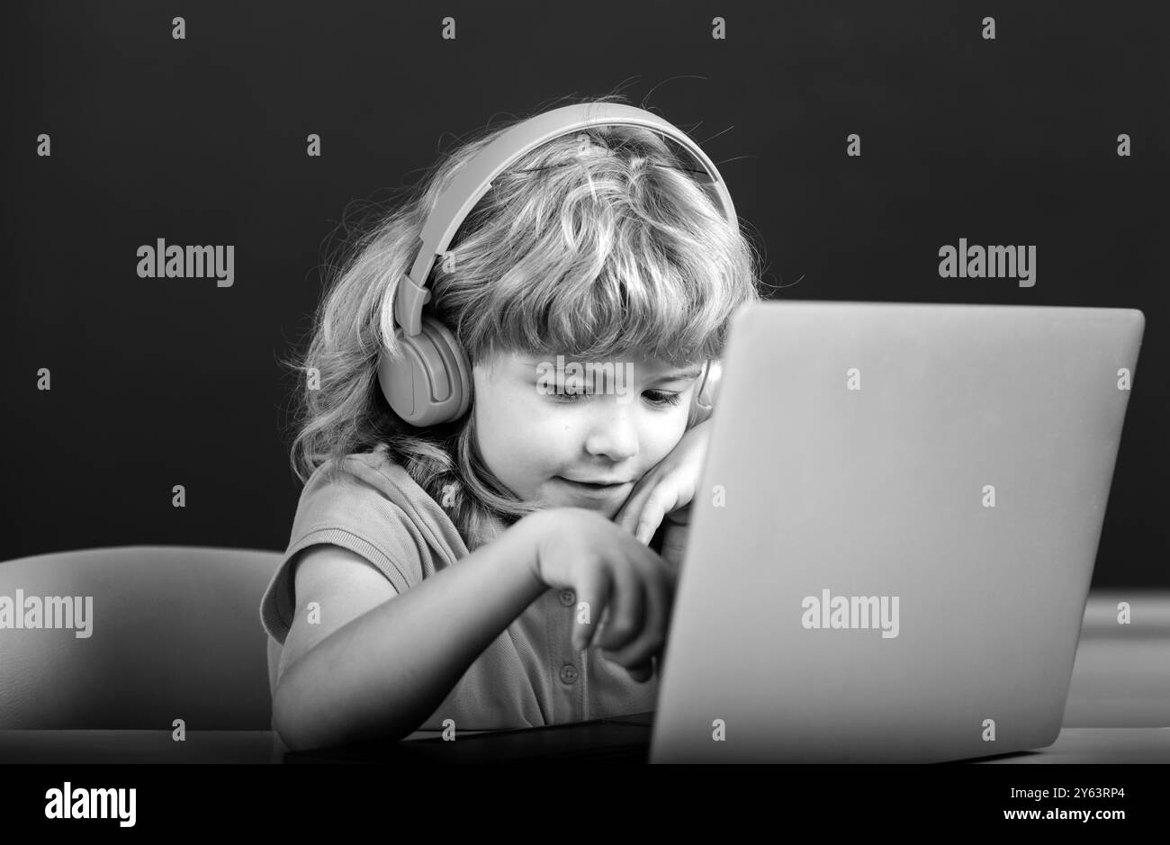 Smart boy dans un casque asseyez-vous au bureau, étudiez en ligne sur un ordinateur portable à l'école, klever Kid porter des écouteurs dans l'apprentissage d'ordinateur portable en utilisant des leçons d'Internet Banque D'Images