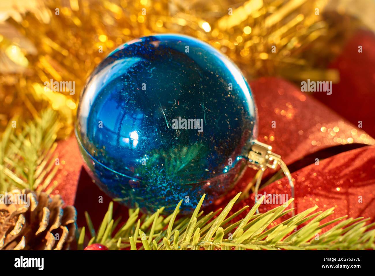 Une décoration de Noël colorée et festive, avec une boule bleu vif entourée d'un noeud rouge étincelant, de pommes de pin et de branches à feuilles persistantes Banque D'Images