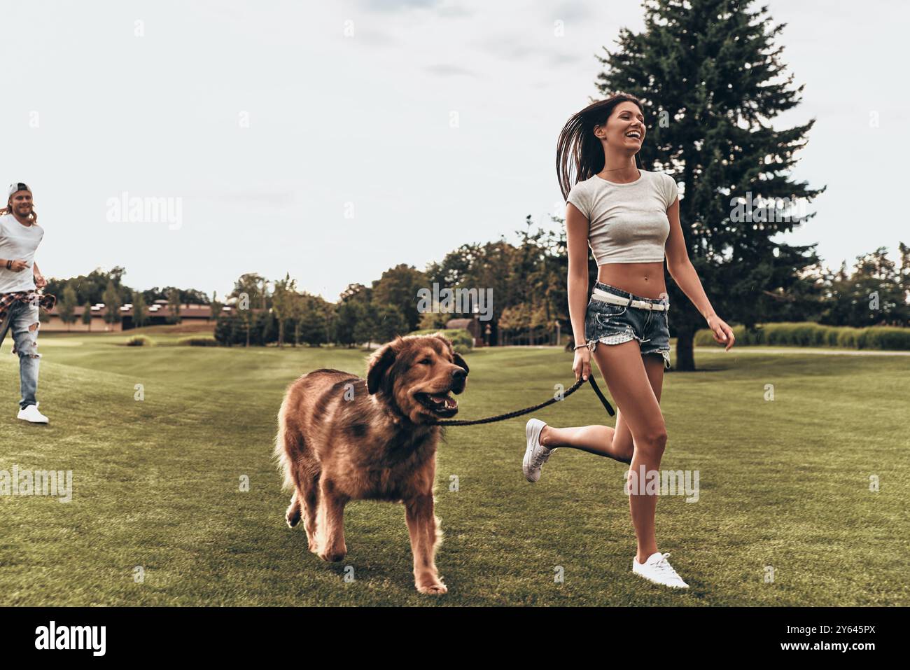 Insouciant et heureux. Pleine longueur de belle jeune femme courir avec un chien tandis que son petit ami court derrière Banque D'Images