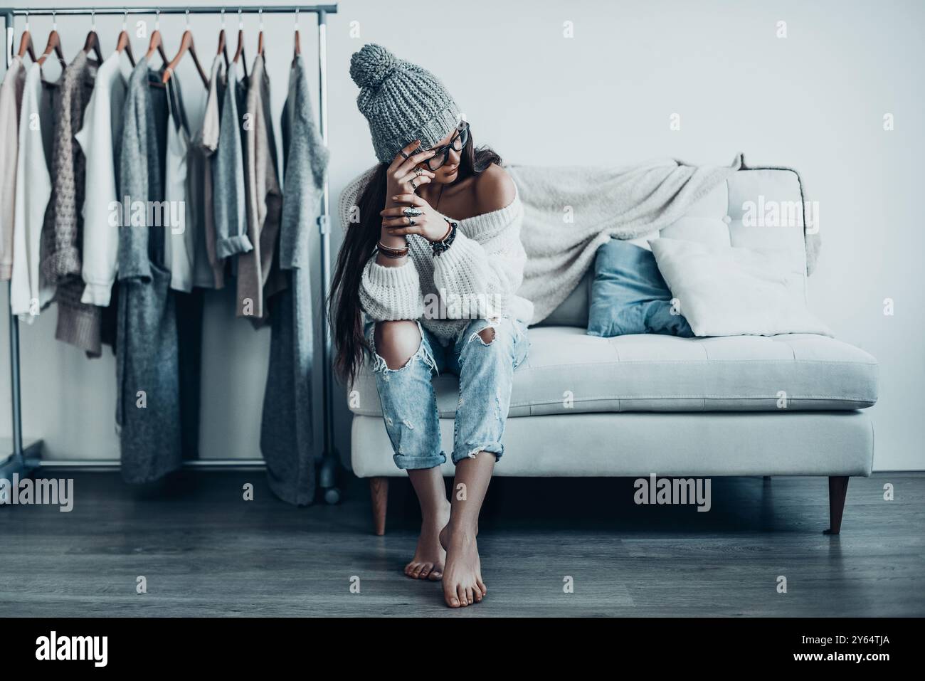 Faire face à des choix difficiles. Jeune femme réfléchie dans des vêtements décontractés touchant sa tête avec la main regardant loin tout en étant assise sur le canapé à la maison près de son vêtement Banque D'Images