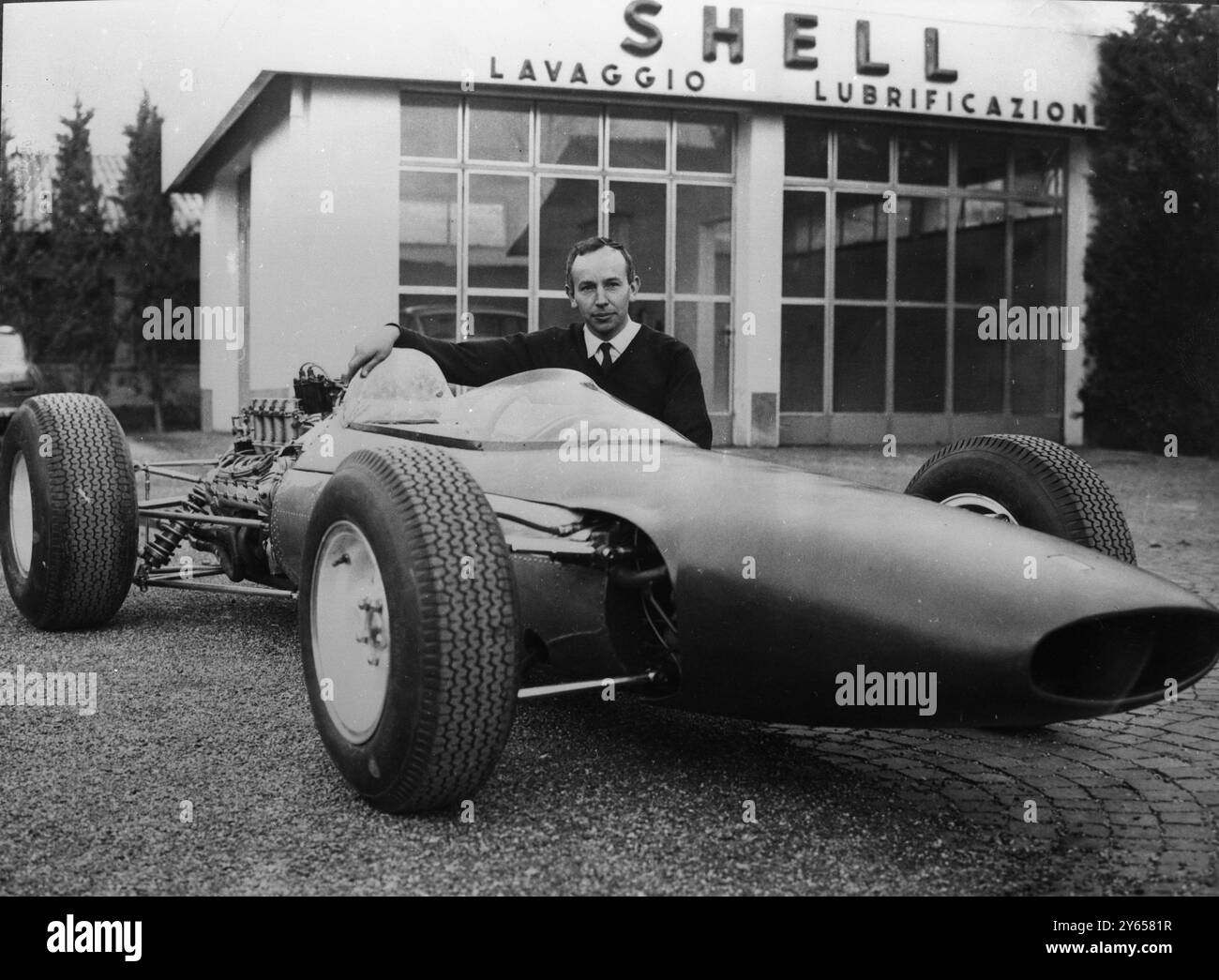 Nouvelle Ferrari Formula One . Modène , Italie : L'as de course britannique John Surtees pose sur le côté de la nouvelle voiture de course Ferrari formule I après qu'elle ait été dévoilée ici . Surtees conduira la voiture lors du Grand Prix de dimanche à Syracuse (Sicile). Il a huit cylindres , moteur arrière à angle de 90 degrés et injection de carburant . 8 avril 1964 Banque D'Images