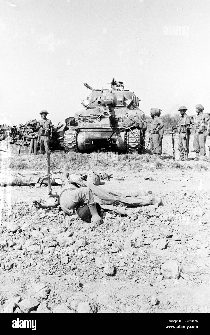 Dograi , Pakistan ; les troupes indiennes se tiennent près d'un char pakistanais fait par les États-Unis capturé , avec un soldat pakistanais mort au premier plan , dans un champ aux abords de Dograi , Pakistan . Cette photo a été prise quelques heures après l'entrée en vigueur du cessez-le-feu indo-pakistanais à l'heure locale , le 23 septembre . Les rapports d'hier indiquaient que les troupes indiennes et pakistanaises se sont livrées à une bataille toute la nuit sur la ligne de cessez-le-feu de l'ONU samedi soir. Les autres rapports indiquent que les deux pays s'accusent mutuellement de violer le cessez-le-feu . 27 septembre 1965 Banque D'Images