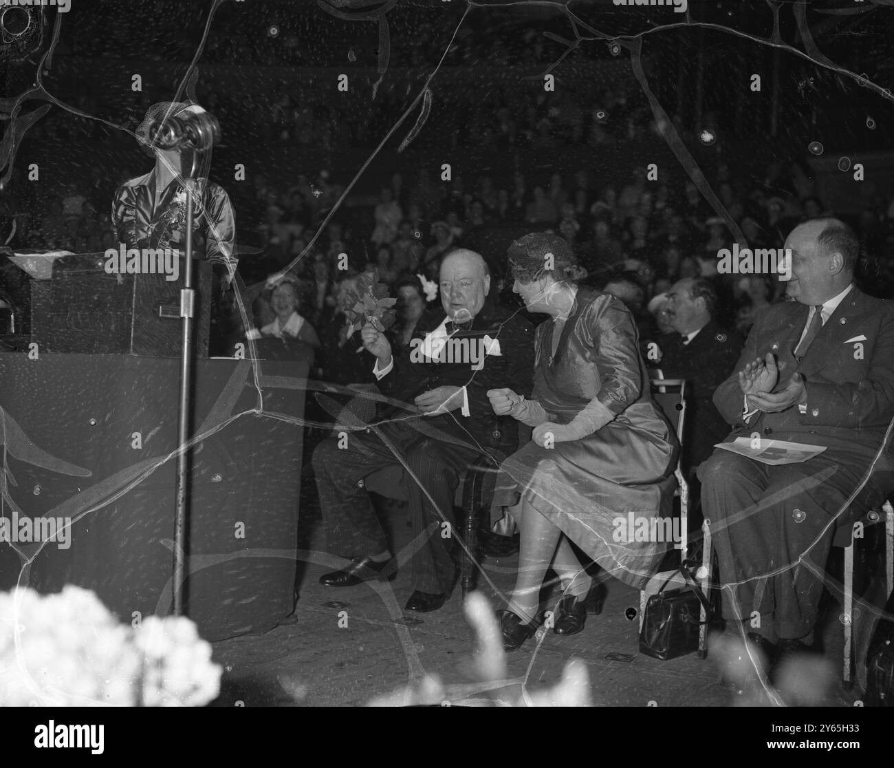 Floral Touch le premier ministre Sir Winston Churchill accroche un bouquet qui lui est présenté par des enfants au Royal Albert Hall , lors d'une réunion de masse tenue conjointement avec la 27e Conférence annuelle des femmes conservatrices . Le premier ministre a adressé la réunion . Assis à côté de lui est Mme Walter Elliot Vice-présidente le 1953-54 27 mai 1954 Banque D'Images