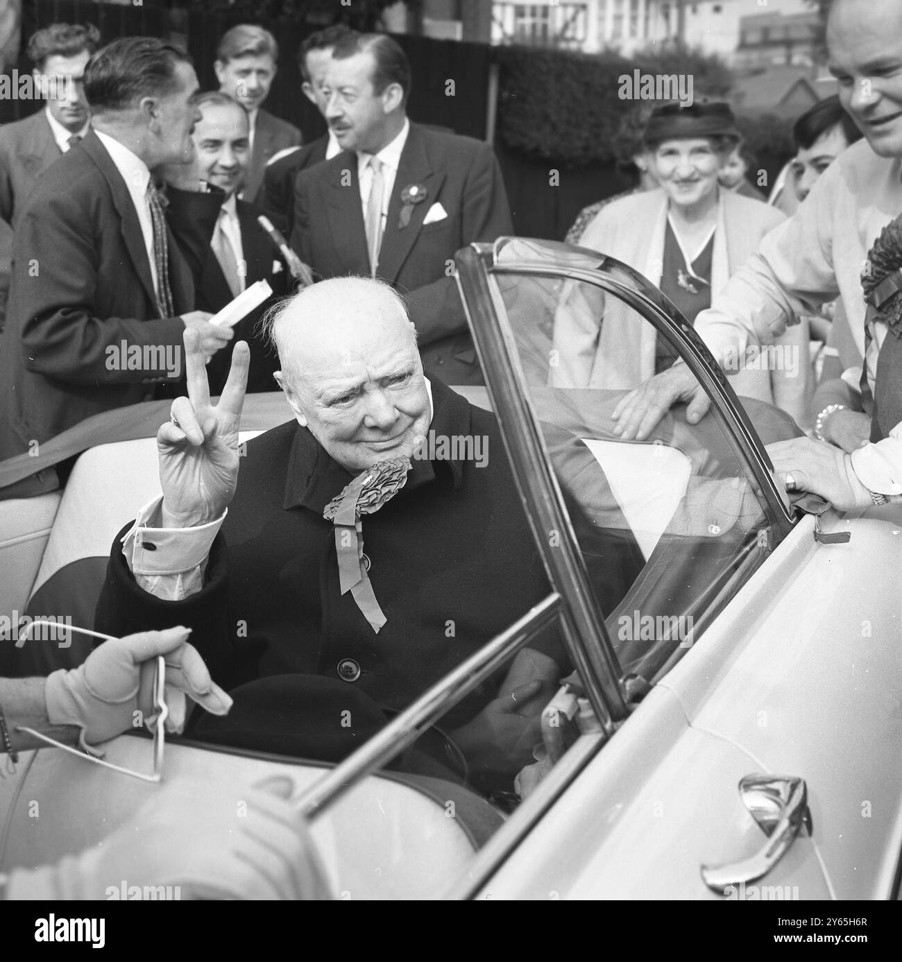 Sir Winston Tours Woodford Sir Winston Churchill donne le signe V avec une rosette bleue dans son revers alors qu'il visite sa circonscription , Woodford , en voiture . 8 octobre 1959 Banque D'Images