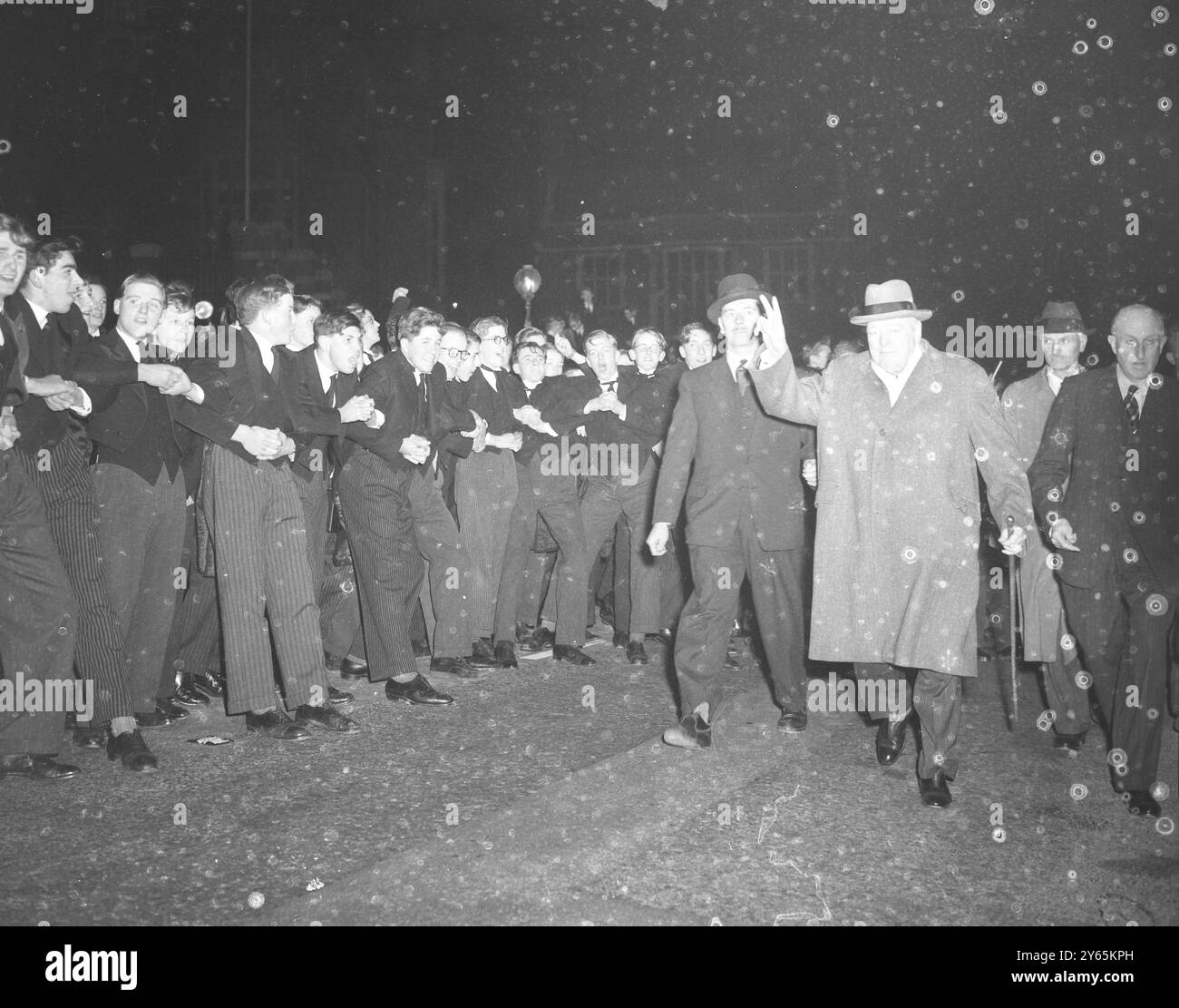 Harrows Distinguished ' Old boy de gros écoliers relient les armes pour retenir les boursiers enthousiastes alors que le premier Ministre Sir Winston Churchill donne son signe de ' victoire ' lors de sa visite annuelle à Harrow , son ancienne école . Sir Winston s'est joint à la chanson de chant annuelle dans la salle de discours. 12 novembre 1954 Banque D'Images