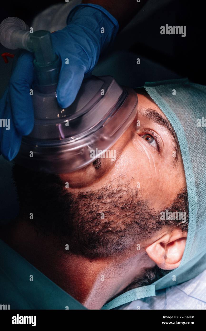 Vue rapprochée détaillée d'un patient masculin recevant un masque d'anesthésie appliqué par un professionnel de santé avant une intervention chirurgicale Banque D'Images