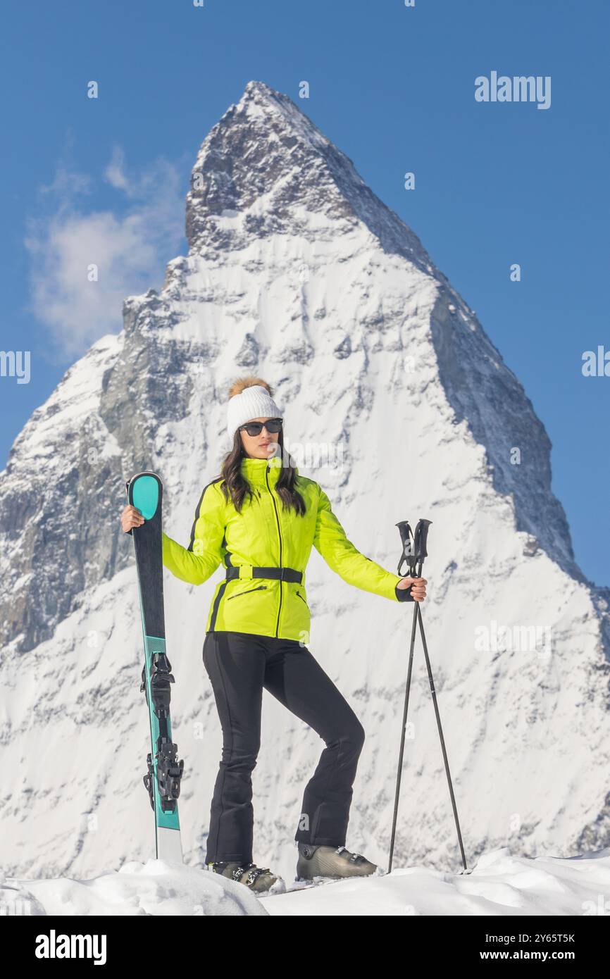 Une skieuse, vêtue d'une veste vert citron vif et d'un équipement de protection, se tient en toute confiance avec son ski sur un magnifique décor alpin, son style Banque D'Images